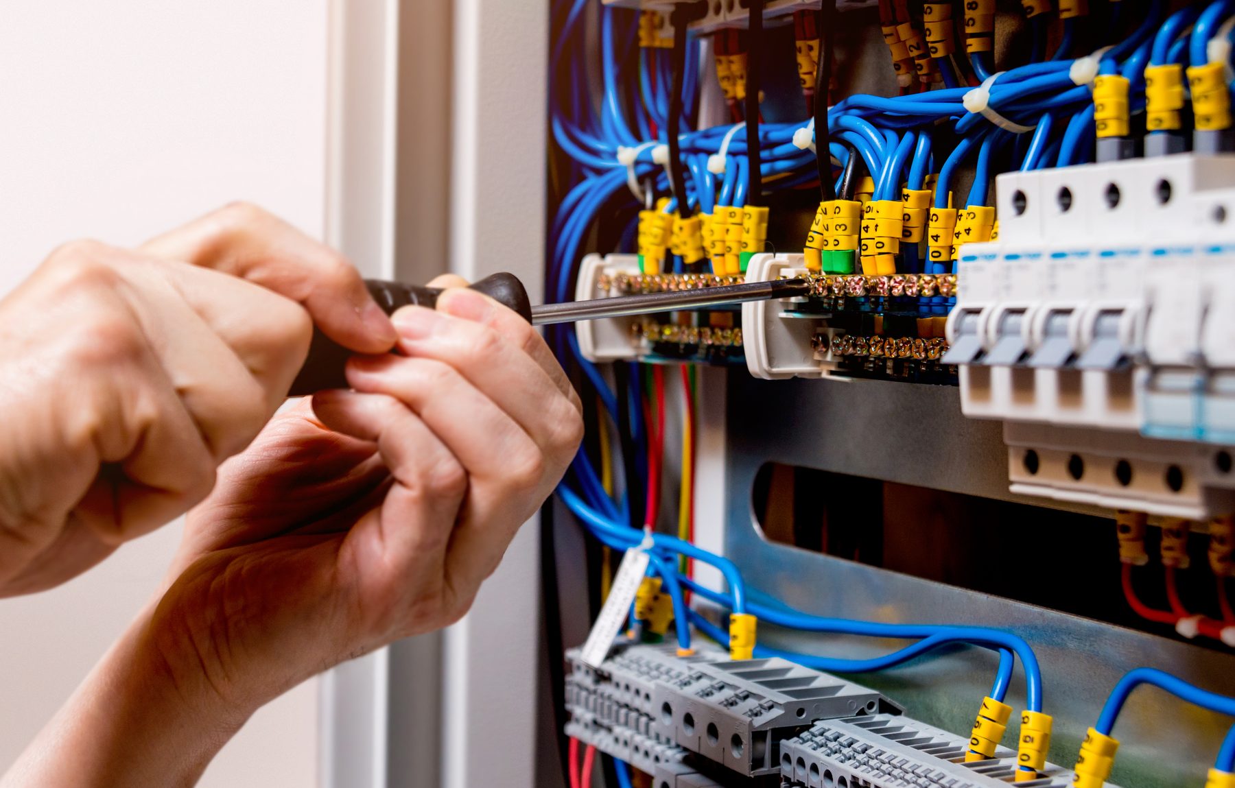 An installer's hands working with a screwdriver inside an electrical panel
